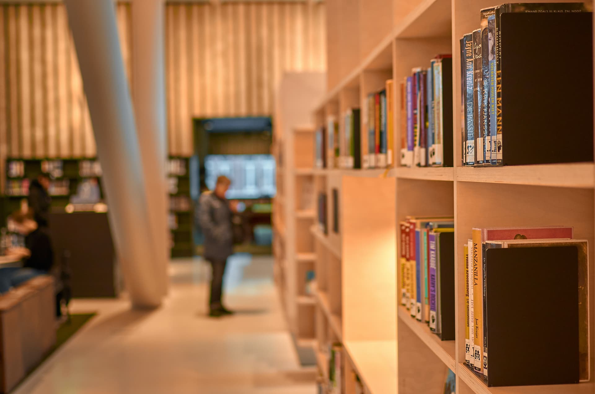 Photo of a man in a library. Man is blurred and the bookshelf is on focus.